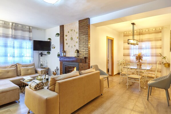 A living room with a sofa, a fireplace, a TV, and a dining area with chairs and a table.
