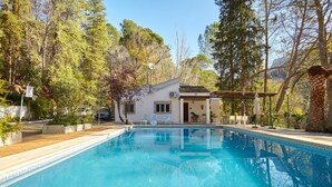 A swimming pool with a house in the background, surrounded by trees.