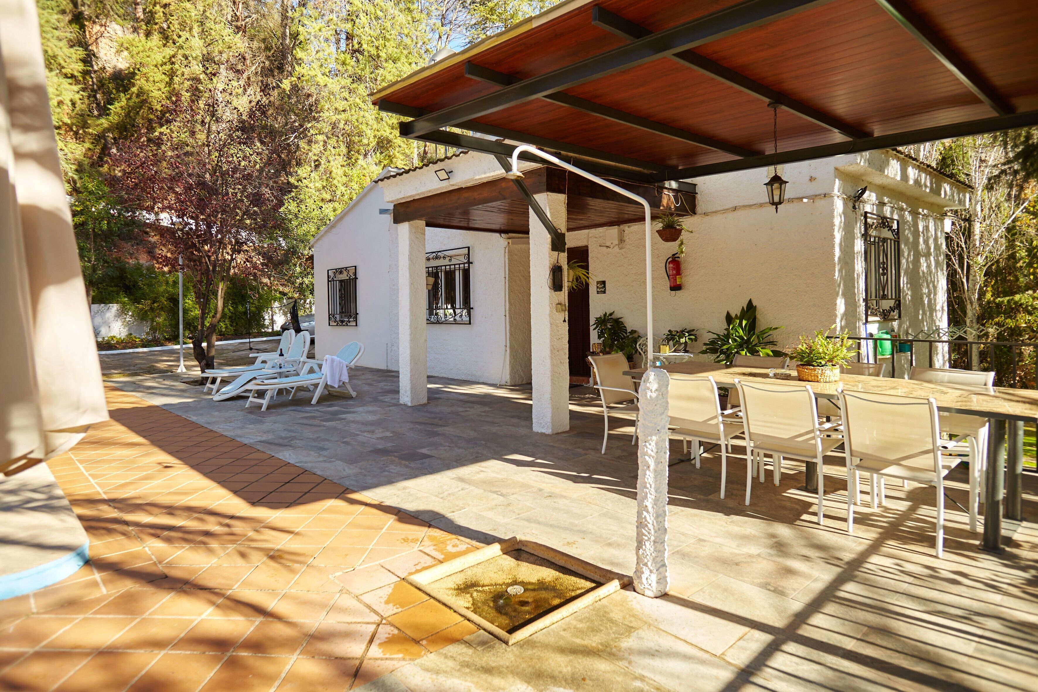 A covered patio area with outdoor seating, a small water feature, and a white building with windows and a door.