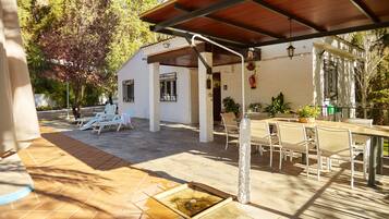 A covered patio area with outdoor seating, a small water feature, and a white building with windows and a door.