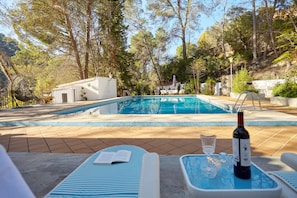 A pool area with lounge chairs, a table with a bottle and glasses, and a book.