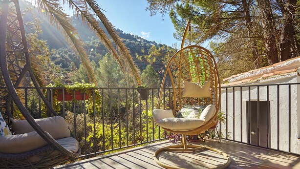 A balcony with wicker chairs, a hanging chair, and a view of a mountainous landscape.