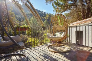 A balcony with wicker chairs, a hanging chair, and a view of a mountainous landscape.