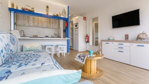 A compact living space with a sofa, a small dining table, a kitchen area, and a mounted television.