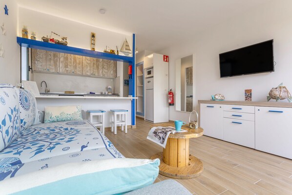 A compact living space with a sofa, a small dining table, a kitchen area, and a mounted television.