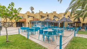 An outdoor patio area with blue tables and chairs, surrounded by a rope barrier.
