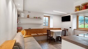 Een modern interieur met een bank, een eettafel, stoelen en een aan de muur bevestigde televisie.
