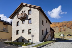 Un edificio de dos pisos con un balcón, una escalera y vistas a un paisaje montañoso.