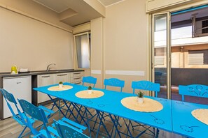 Une cuisine compacte équipée d’un évier, d’un petit réfrigérateur et d’un coin repas avec des chaises et une table bleues.