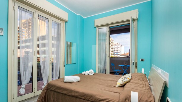Une chambre à coucher avec un lit, des rideaux, une fenêtre et une vue sur les bâtiments environnants.