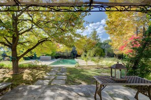 Un jardín con un sendero de piedra, una piscina y una pérgola con un farol.