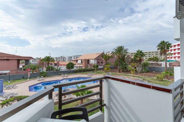 A balcony with a view of a swimming pool, palm trees, and surrounding buildings.