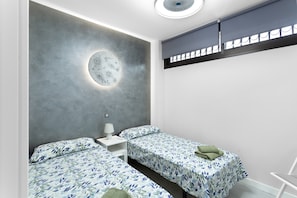 A modern bedroom with two beds, a circular light fixture, and a skylight.