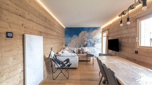 A cozy room with wooden walls, a sofa, a chair, a TV, and a window with a snowy view. - Apartment 'Le Chappart - Carroz D'Arâches' with Mountain View, Private Terrace and Wi-Fi (Arâches-la-Frasse)