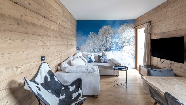A cozy room with a wooden interior, a sofa, a chair, a small table, and a TV. - Apartment 'Le Chappart - Carroz D'Arâches' with Mountain View, Private Terrace and Wi-Fi (Arâches-la-Frasse)