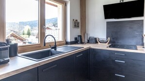 A modern kitchen with a large window, a built-in stove, and a flat-screen TV. - Apartment 'Le Chappart - Carroz D'Arâches' with Mountain View, Private Terrace and Wi-Fi (Arâches-la-Frasse)