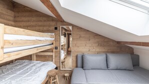 A loft bedroom with a sloped ceiling, wooden walls, a bunk bed, a sofa, and a small stool. - Apartment 'Le Chappart - Carroz D'Arâches' with Mountain View, Private Terrace and Wi-Fi (Arâches-la-Frasse)