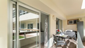A modern kitchen with a dining area, a sliding glass door leading to a balcony, and a small window with a plant.