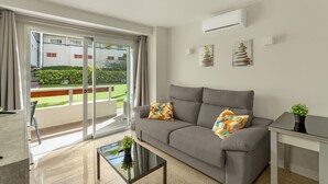 A modern living room with a grey sofa, a glass door leading to a balcony, and a small table with a plant.