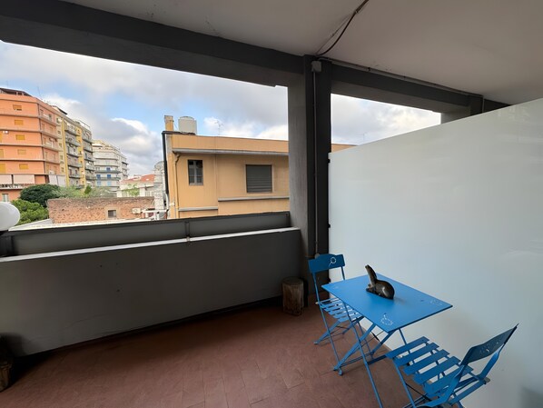 Un balcón con mesa y sillas, vistas a edificios y una ventana.