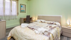Hotellihuone, jossa on sänky, työpöytä, tuoli, yöpöytä ja ilmastointilaite.