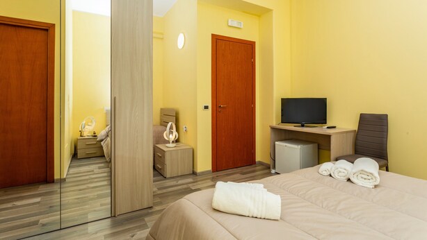 Ein Hotelzimmer mit Bett, Fernseher, Schreibtisch, Stuhl, Spiegel und Kleiderschrank.