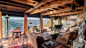 A cozy room with a stone fireplace, wooden ceiling beams, a comfortable sofa, and a view of mountains. - Holiday Home 'Casa Do Gêres' with Lake View, Private Pool and Wi-Fi (Gêres)