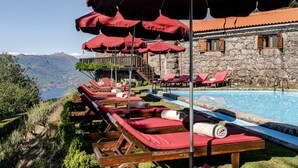 A poolside area with sun loungers and umbrellas, a stone building, and a view of mountains. - Holiday Home 'Casa Do Gêres' with Lake View, Private Pool and Wi-Fi (Gêres)