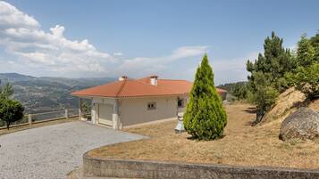 A house with a red-tiled roof, a paved driveway, and a view of the surrounding landscape.