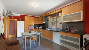 A modern kitchen with wooden cabinets, a dining table with chairs, a refrigerator, and a washing machine.