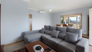 A living room with a grey sectional sofa, a wooden coffee table, and a view through an open door to an outdoor area.