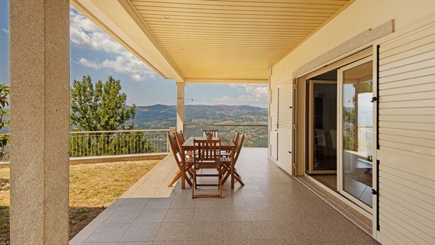 A covered patio with a table and chairs, a sliding glass door, and a view of the landscape.