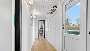 A hallway with white walls and wooden flooring leading to a door with a view of a backyard.