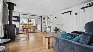 A spacious living room with a large wooden table, a grey sofa, and a black fireplace.