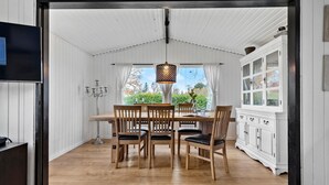 A dining area with a wooden table and chairs, a chandelier, and a view of greenery outside.