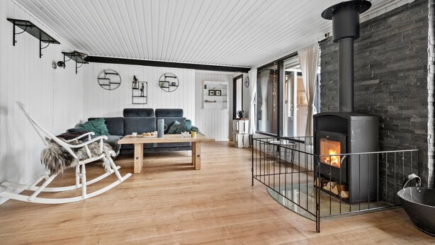 A cozy living room with a wooden floor, a black sofa, a rocking chair, a coffee table, and a fireplace with a stone wall.