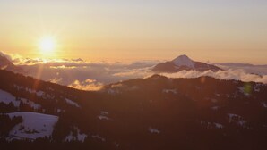 A mountain landscape with a prominent peak, forested areas, and a valley.