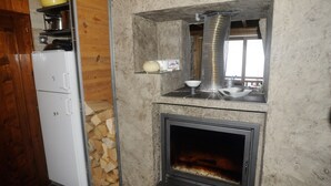 A compact kitchen with a wood-burning stove, a white refrigerator, and a small shelf with a yellow bowl.
