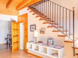Un escalier avec des marches en bois et des rampes noires, une console blanche ornée de livres et d’objets décoratifs, et une porte en bois avec un panneau de verre.