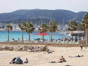 Ein Strand mit Palmen, einem roten Sonnenschirm und entspannten Menschen.