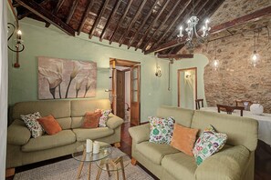 A cozy living room with two sofas, a glass coffee table, and a stone wall. - Casa Isabel: An Authentic Canarian House with Terraces and Mountain Views (Santa Brigida)