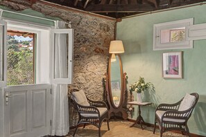A room with a stone wall, two wicker chairs, a floor lamp, and a small table with a vase of flowers. - Casa Isabel: An Authentic Canarian House with Terraces and Mountain Views (Santa Brigida)