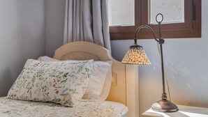 Una cama con ropa de cama floral, una lámpara de noche y una ventana con cortinas.