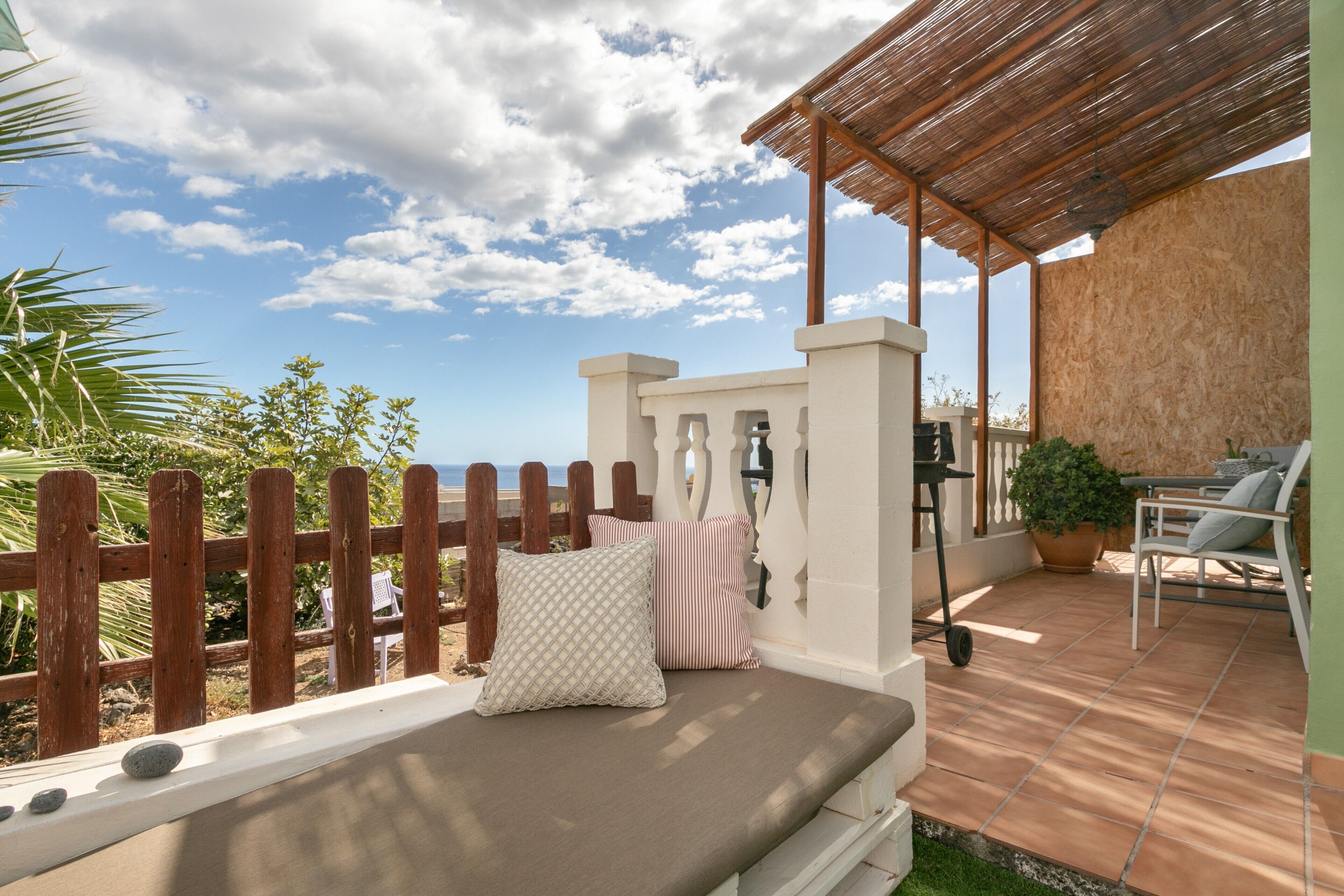 A patio with a cushioned seating area, a wooden fence, and a view of the sea.