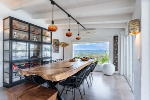 Un comedor moderno con una gran mesa de madera, sillas de mimbre negro y vistas del paisaje a través de un ventanal.