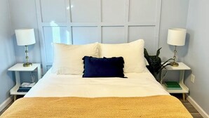 Un dormitorio ordenado con una cama grande, dos mesitas de noche con lámparas y una ventana con persianas.