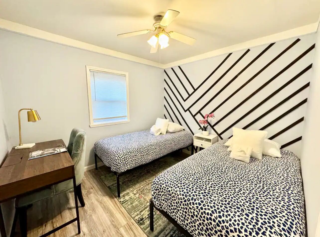 A bedroom with two beds, a desk, a chair, a ceiling fan, and a window.