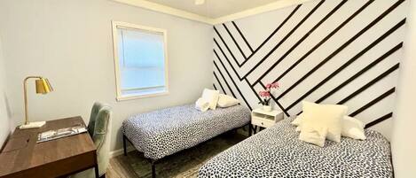 A bedroom with two beds, a desk, a chair, a ceiling fan, and a window.