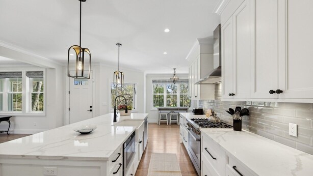 Cocina moderna con armarios blancos, una isla grande e iluminación colgante.