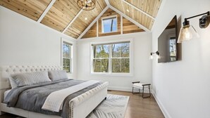 Un dormitorio con una cama grande, techo de madera y ventanas amplias.